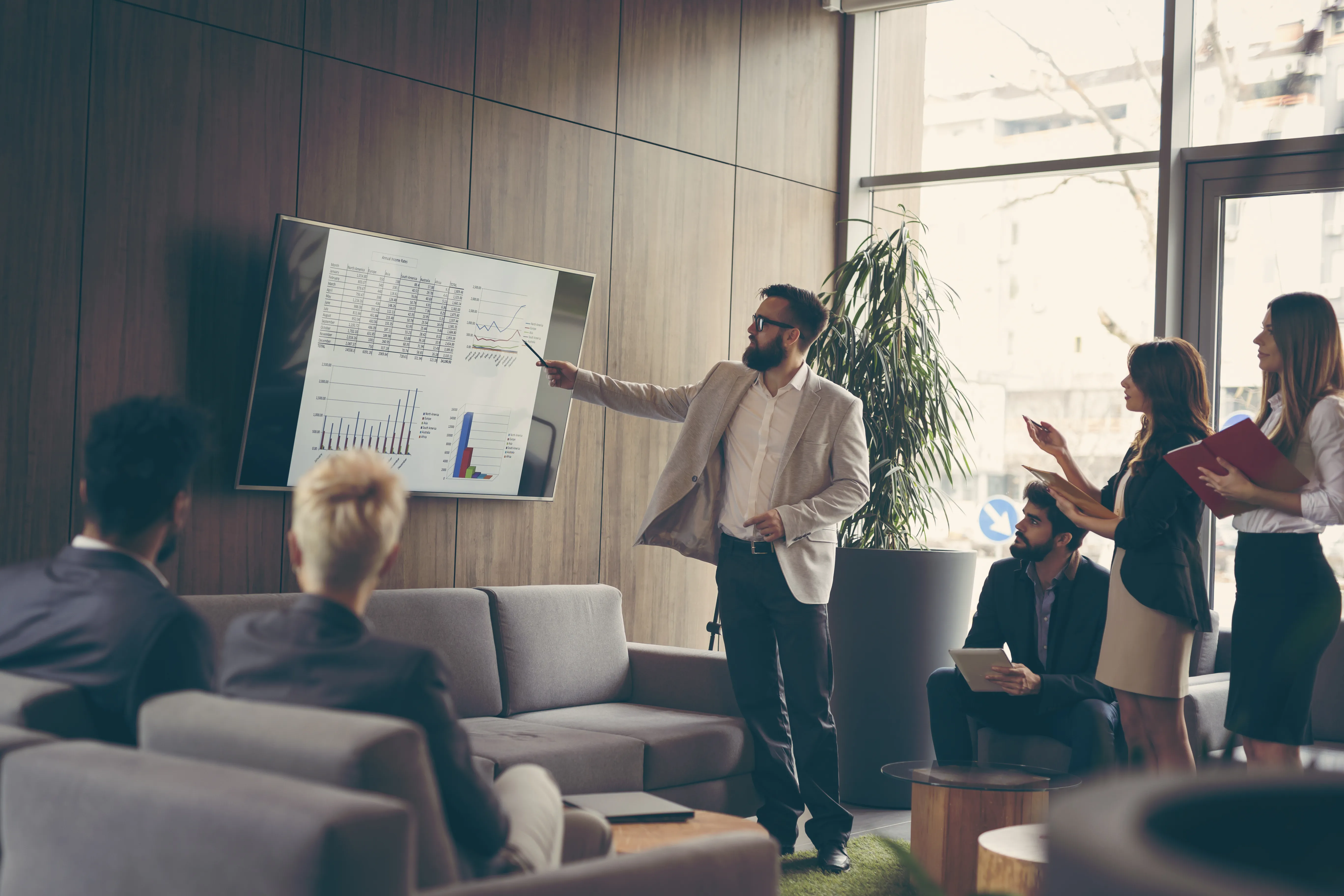 Business meeting with presenter pointing at data on a large screen