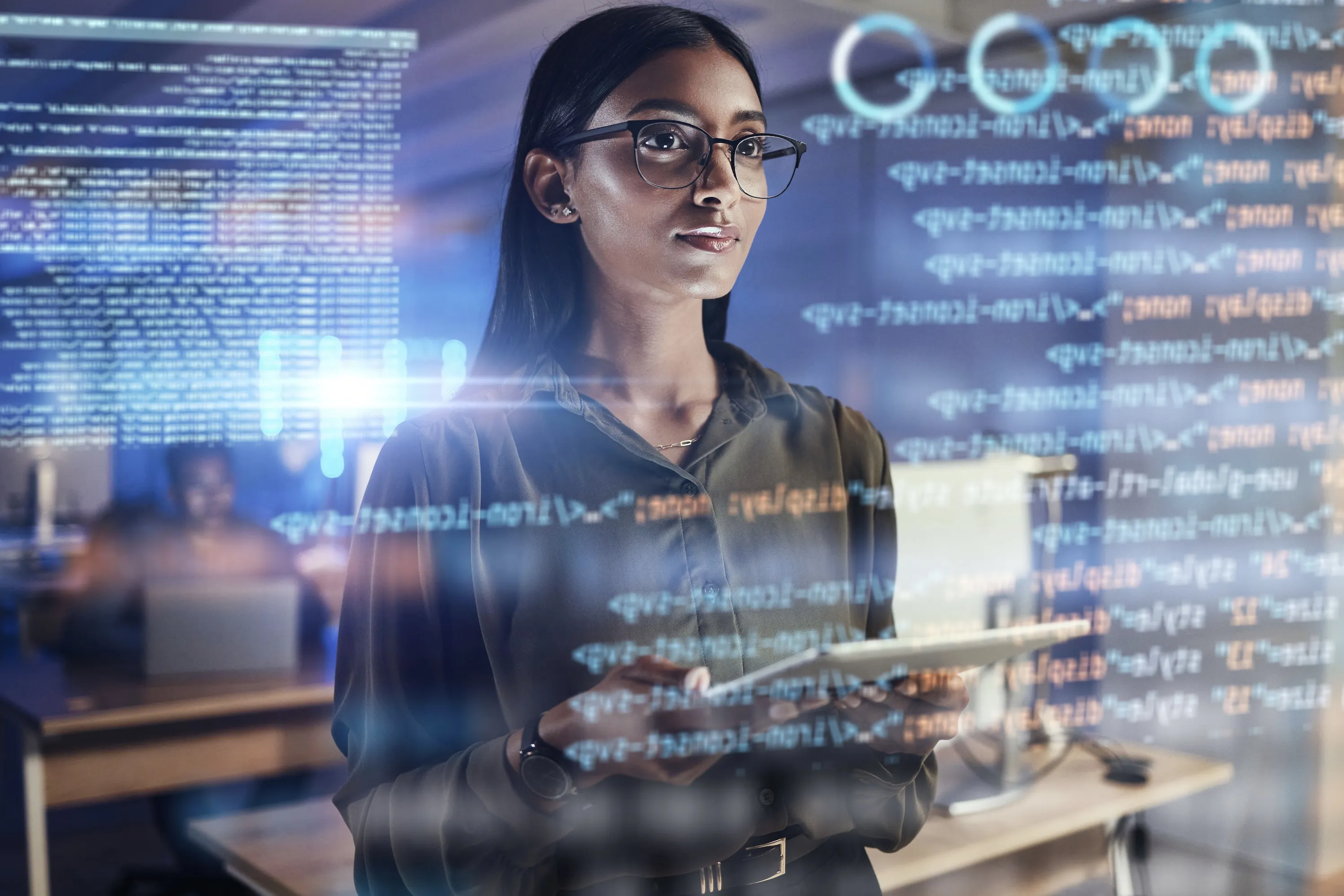 Woman in glasses analyzing data on digital screens in a tech environment.